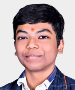 Portrait of a smiling boy wearing a denim jacket and white shirt, with a red tilak on his forehead, against a light background.