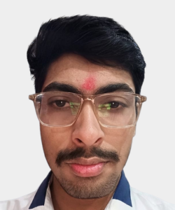 Close-up of a man with short dark hair, glasses, and a red tilak on his forehead.